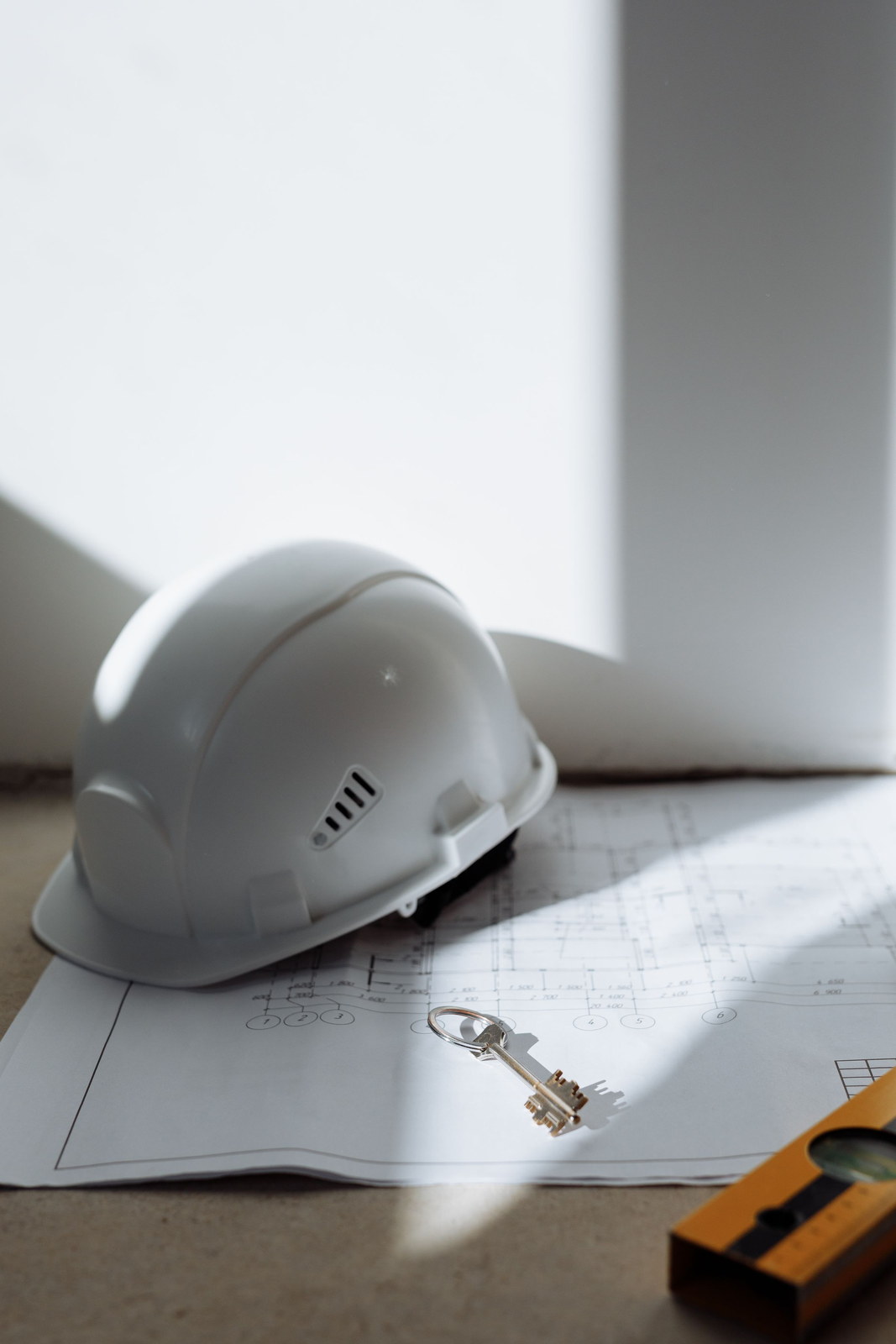 A white hard hat and a house key resting on architectural floor plans