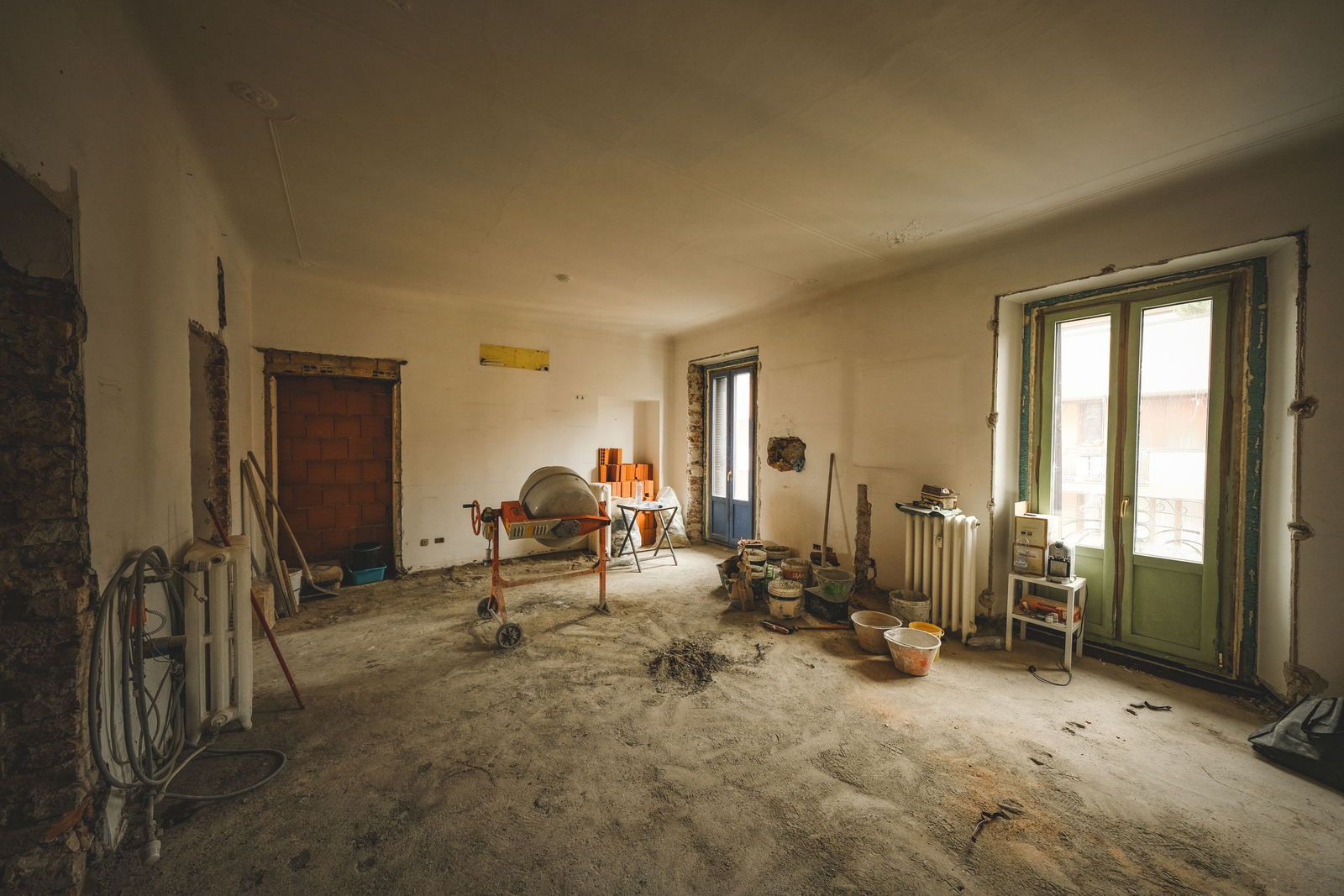 An empty room mid-refurbishment with a cement mixer, buckets and exposed brickwork