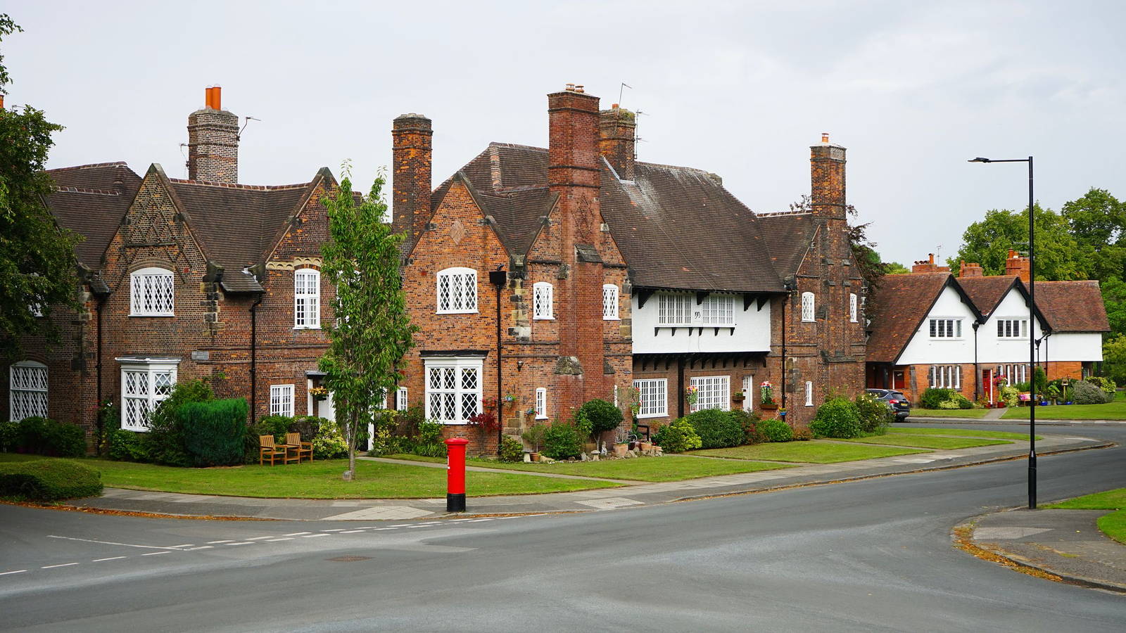 Red-brick houses with white lattice windows and a red pillar box on a UK residential street
