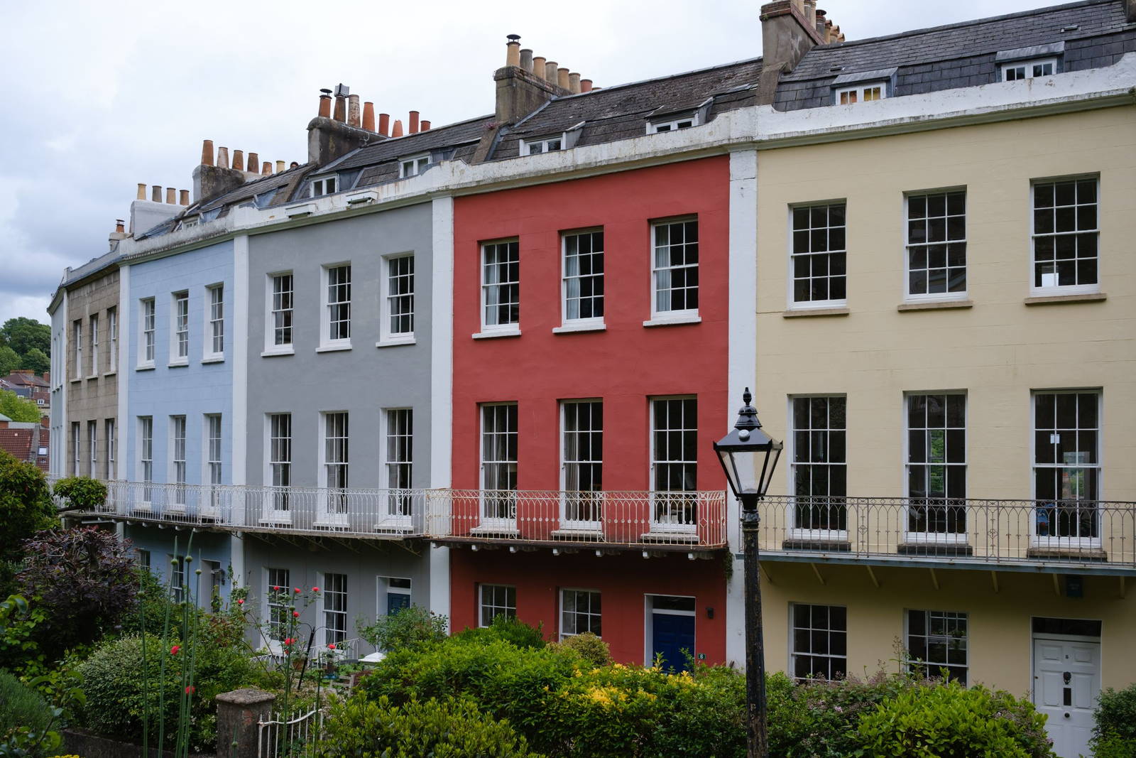 A row of colourful UK terraced houses with white sash windows and iron balconies